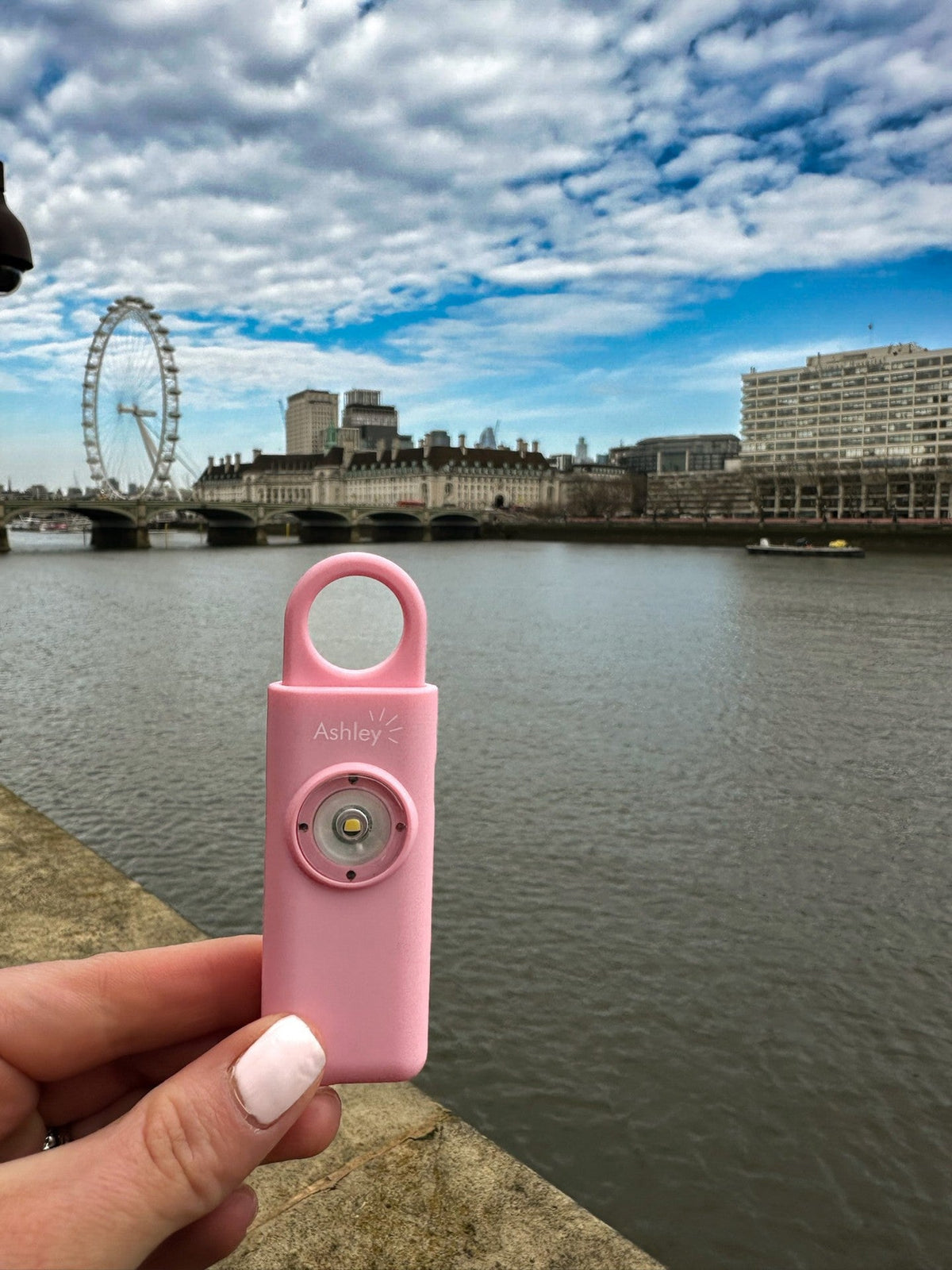 Pink Ashley personal alarm held by the River Thames in London